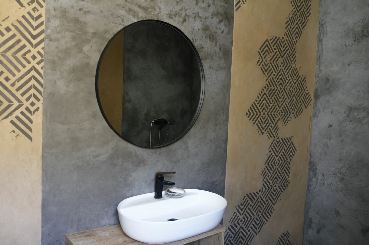 Baño con pared de microcemento gris, espejo redondo y lavabo